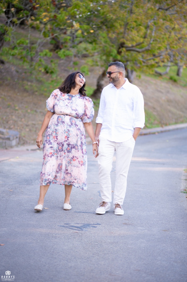A couple laughing and walking hand in hand along a tree-lined path