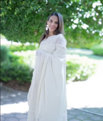 A woman in a flowing white outfit smiling in a garden