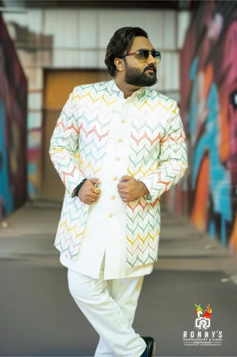 A man in a colourful embroidered jacket standing in front of a graffiti wall