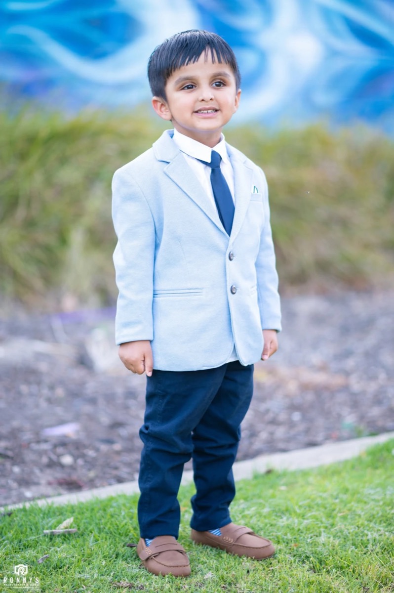 A young boy in a light blue blazer and tie standing on the grass